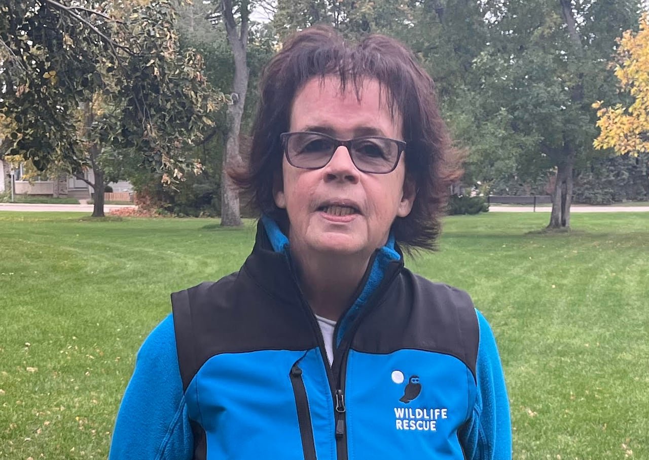 A woman stands in a park wearing a badge that says "Wildlife Rescue."